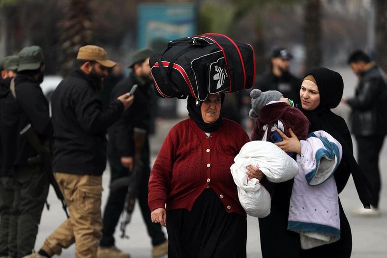 Une femme portant un gros sac sur la tête et une autre femme tenant un enfant marchent dans une rue d'Alep, en Syrie, alors que des civils déplacés évacuent en raison de l'escalade des hostilités.